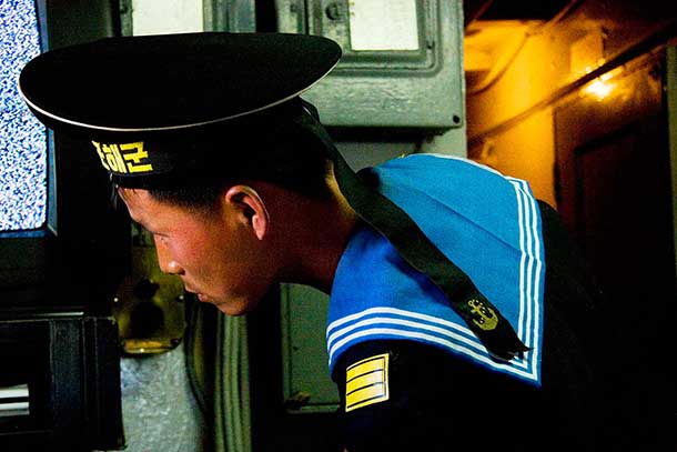 Visitors to the Pueblo, a US ship captured in the 1960s, watch a film documenting the capture. The DVD kept getting stuck, necessitating the help of various attendants